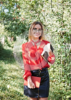 Young attractive woman with blond short hair, wearing red shirt and black skirt, holding books in her hands. Three-quarter