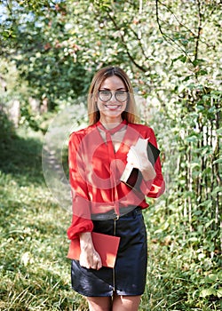 Young attractive woman with blond short hair, wearing red shirt and black skirt, holding books in her hands. Three-quarter