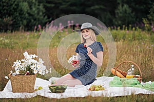 Young attractive woman in a blue dress at an outdoor picnic. A basket with daisies, watermelon, strawberries and a glass