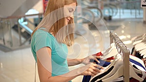 Young attractive woman choosing clothes at shop. Shopping in mall, sales time. Consumerism concept