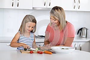 Young attractive woman cooking together with her sweet beautiful blond little 6 or 7 years old daughter smiling happy preparing sa