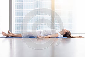 Young attractive woman in Corpse pose against floor window