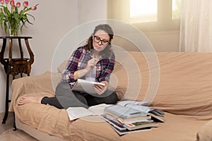 Young attractive woman with dark curly hair sitting at the couch with notebook and books