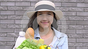 A young attractive woman in a denim jacket and hat is holding a package with products while having a good mood and