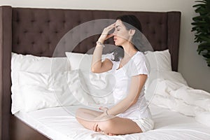 Young attractive woman doing nadi shodhana pranayama pose on bed