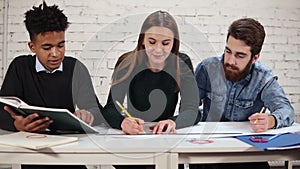 Young attractive woman is drawing a plan using straightedge and paper. Happy diverse group of collegues working on