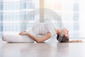 Young attractive woman in Fish pose against floor window