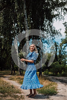 A young attractive woman with flowers in her hands walks through the forest