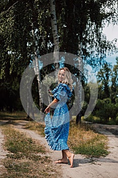 A young attractive woman with flowers in her hands walks through the forest