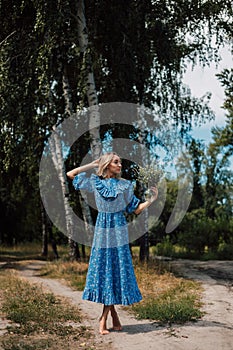 A young attractive woman with flowers in her hands walks through the forest