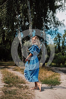 A young attractive woman with flowers in her hands walks through the forest