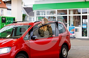 Young attractive woman gets out of her car by gas station to refill car with petrol or gas. People refuel gasoline