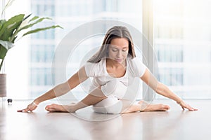 Young attractive woman in Gomukasana pose against floor window