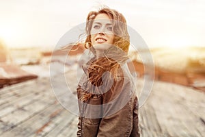 Young attractive woman with good mood enjoying beautiful city landscape while standing on a roof of building, charming smiling hip