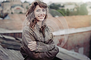 Young attractive woman with good mood enjoying beautiful city landscape while standing on a roof of building, charming smiling hip