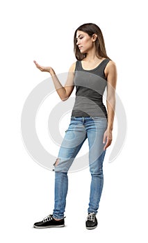 Young attractive woman in gray sleeveless top and blue jeans standing in half-turn with right arm bent at elbow and