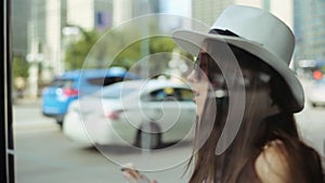 Young attractive woman in hat calls on phone at bus stop next to road.