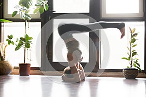 Young attractive woman in headstand pose, home interior backgrou