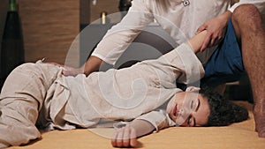 Young attractive woman with her eyes closed is receiving thai massage. Male thai massagist is stretching woman`s hand