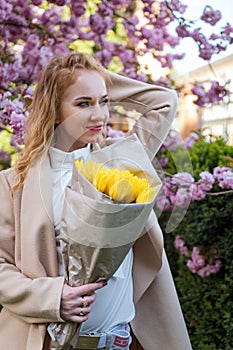 Young attractive woman holding bouquet of yellow tulips in park. Woman with flowers outside waiting for someone. Vertical frame