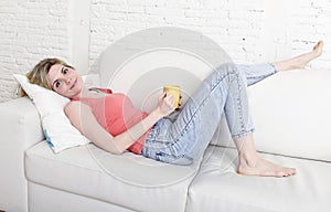 Young attractive woman holding cup of coffee sitting on sofa couch at home smiling happy