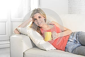 Young attractive woman holding cup of coffee sitting on sofa couch at home smiling happy