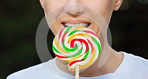 Young attractive woman is holding a multicolored, round lollipop near the mouth