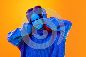 Young attractive woman in knitted wool winter sweater suffering from headache over gradient background in neon light.