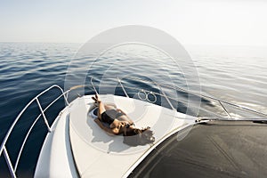 Young attractive woman lies and sunbathing on the bow of a luxury yacht