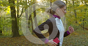 Young attractive woman listening music in the earphone while running in the city park.