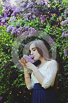 Young attractive woman in long dress in spring garden with bouquet of purple lilacs. Sunset light. Spring background. Internationa