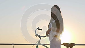 Young attractive woman with long hair is having a good time at sea. Female with a bicycle