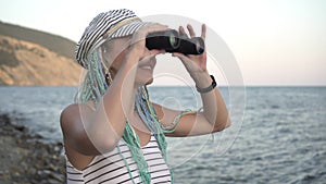 Young attractive woman looks through binoculars towards the sea