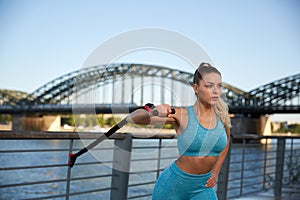 Young attractive woman makes fitness workouts on the promenade