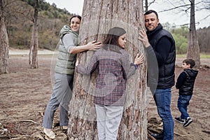 Young attractive woman, man and pretty teenage girl are hugging large cypress trunk