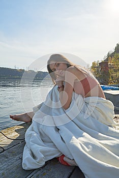 A young attractive woman of model appearance rests under a blanket on a pier. long hair