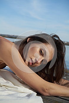 A young attractive woman of model appearance rests under a blanket on a pier. long hair