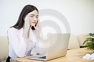 Young attractive woman at modern office desk, working on laptop, massaging temples to forget about constant headaches, noisy loud