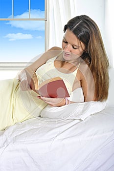 Young attractive woman in nightgown lying relaxed on bed reading novel book