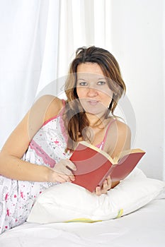 Young attractive woman in nightgown lying relaxed on bed reading novel book