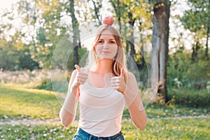 Young attractive woman outdoor holding red apple on her head, giving thumbs up and looking to camera with smile