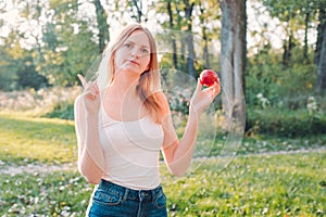 Young attractive woman outdoor holding red apple and thinking about something on the blur nature background. Lunch in