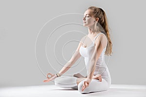 Young attractive woman in Padmasana pose with mudra, grey studio