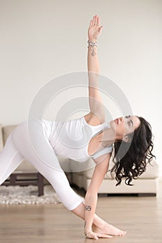 Young attractive woman in Parivrtta Trikonasana pose, the living