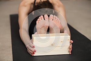 Young attractive woman in paschimottanasana pose with block, gre