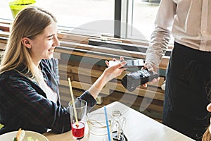 Young attractive woman paying in cafe with contactless smartphone payment