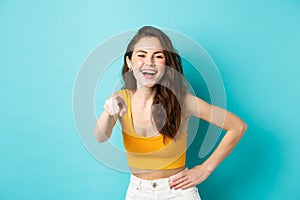 Young attractive woman with perfect body in summer clothes, laughing and smiling, pointing finger at camera, choosing