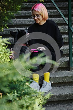 A young attractive woman with pink hair is sitting on the stairs in spring park with her Blue Heeler. Australian cattle