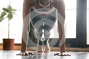 Young attractive woman in Plank pose, home interior background