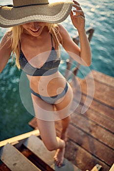 Young attractive woman posing and standing on wooden jetty by blue water. Summer vacation. Holiday, fun, well being, lifestyle